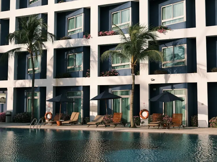 Modern luxury hotel facade in Portugal with a pool, lounge chairs, and palm trees, showcasing premium property suitable for Golden Visa investment.