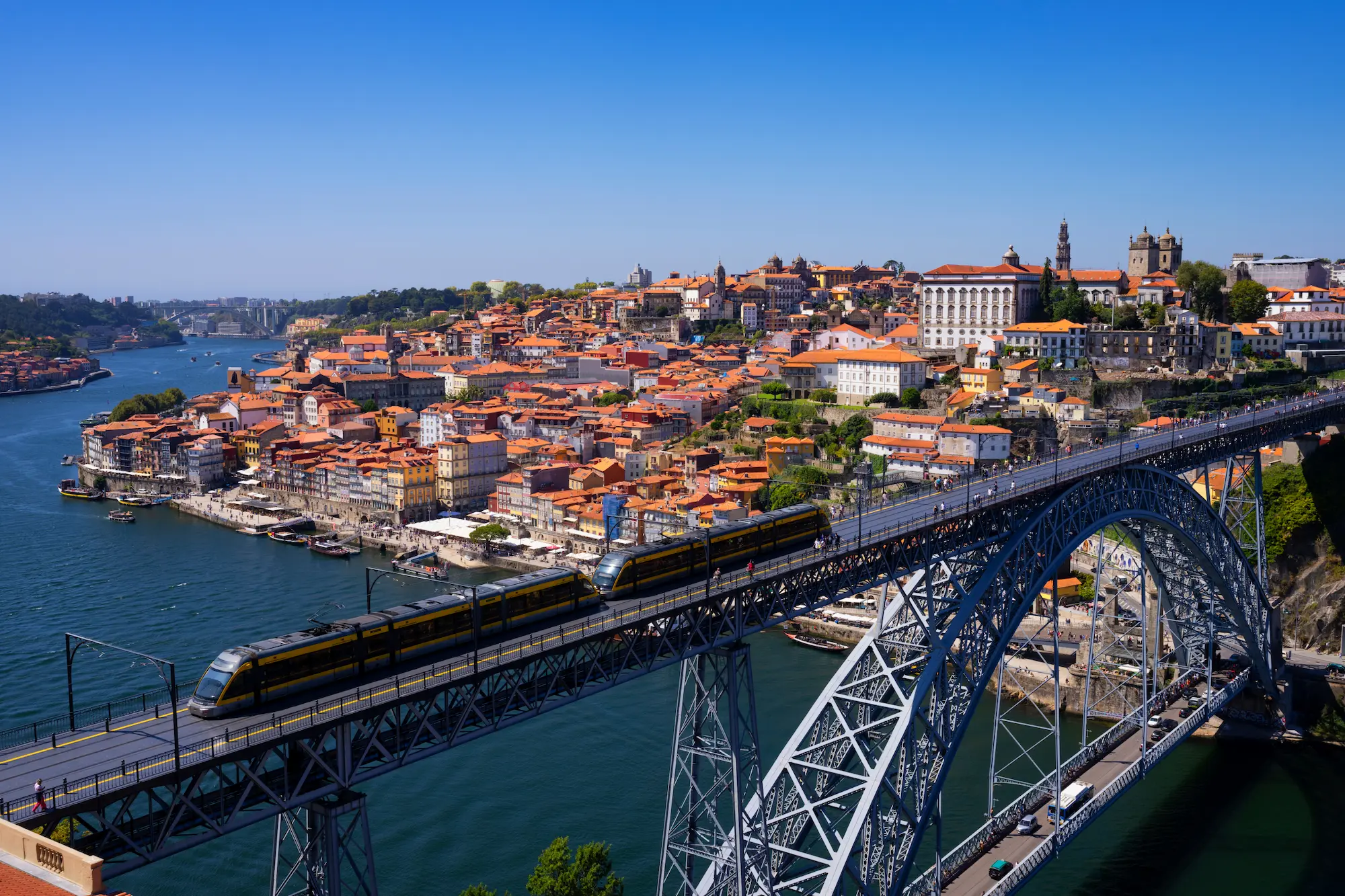 Iconic Dom Luís I Bridge in Porto with the metro crossing the Douro River above the historic Ribeira district, showcasing the city's infrastructure and UNESCO beauty.